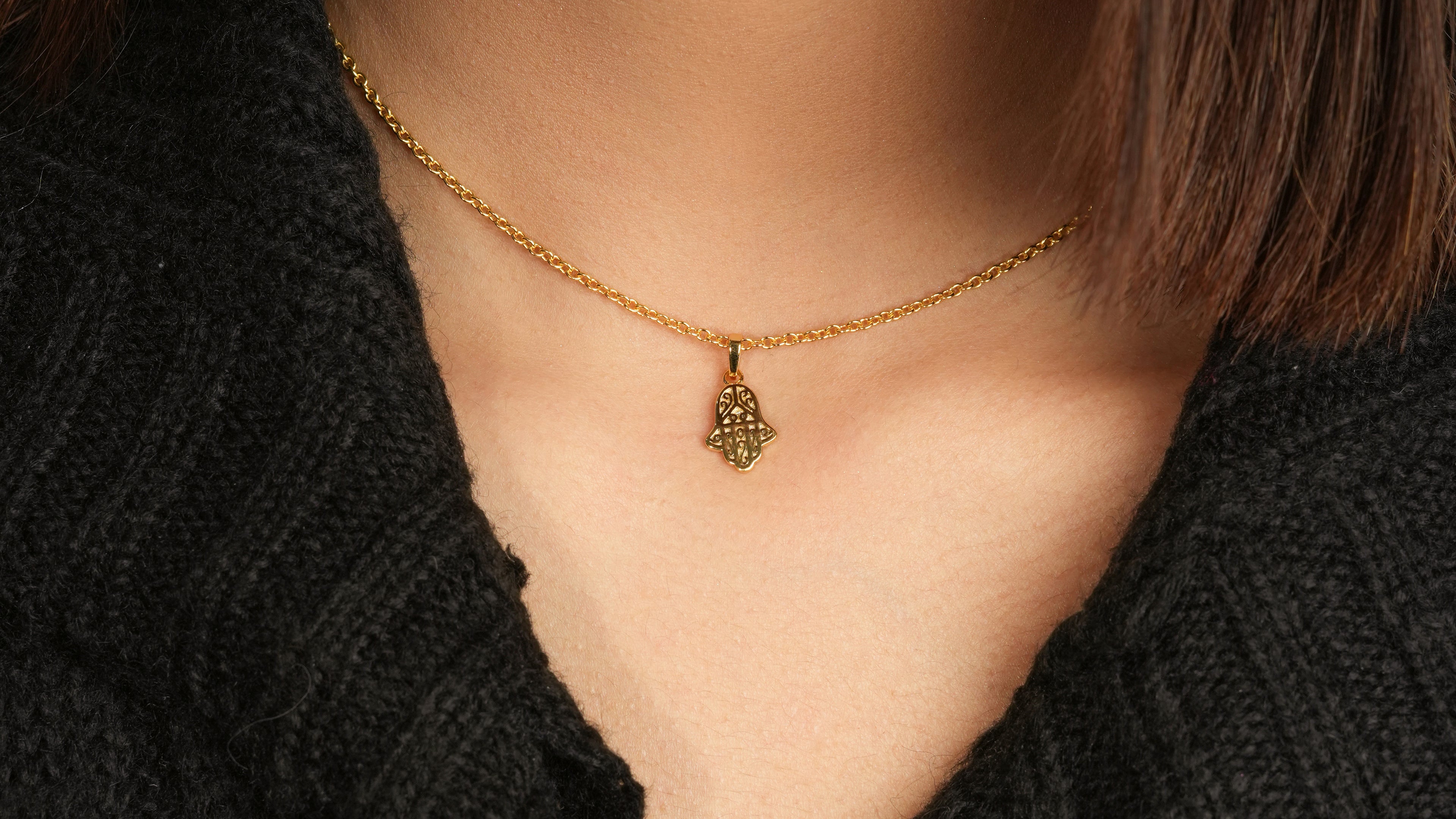 Person wearing small gold hamsa necklace